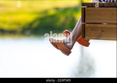 Eine Frau sitzt am Rand eines Steges und schwingt ihre Beine über das Wasser des Sees Stockfoto