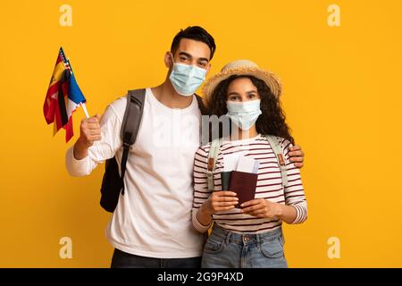 Pandemie Reist. Junges Paar Mit Medizinischen Masken, Die Pässe Und Internationale Flaggen Tragen Stockfoto