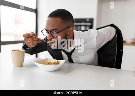 Schwarzer Mann eilt zur Arbeit und frühstückt zu Hause Stockfoto