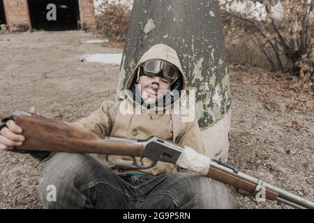 Wandernder Junge. Junge mit einer Waffe. Junge geht zu einem verlassenen Gebäude. Junge steht vor einem Gebäude. Post-Apokalypse. Mann, der zu Fuß in einem Stockfoto