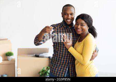 Glückliche afroamerikanische Ehegatten demonstrieren Hausschlüssel an der Kamera und umarmen Stockfoto