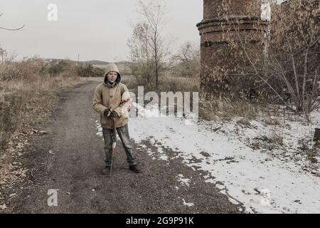 Wandernder Junge. Junge mit einer Waffe. Junge geht zu einem verlassenen Gebäude. Junge steht vor einem Gebäude. Post-Apokalypse. Mann, der zu Fuß in einem Stockfoto