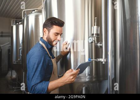 Mann mit Gadget arbeitet in der Fabrik mit mobilen App, steuert Ausrüstung Stockfoto