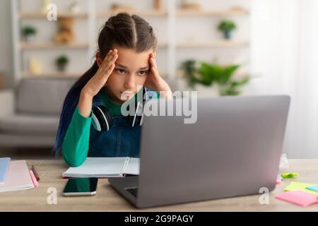 Müde Schulmädchen tun Hausaufgaben Grabbing ihren Kopf mit pc Stockfoto