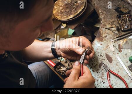 Ein Juwelier entfernt in einer Werkstatt Details von einem Goldring mit Edelsteinen Stockfoto