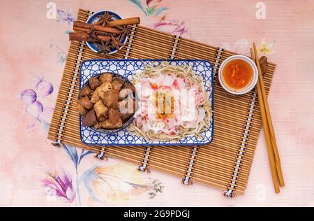 Chinesische gedämpfte Reisnudeln und Bohnensprossen werden mit gebratenes Schweinefleisch, Tofu, knuspriges Tintenfisch in süßer Sojasauce in Keramikplatte mit eingelegter Chili serviert. Asiatisch Stockfoto