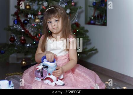 Kind Mädchen in rosa Kleid ist nicht zufrieden mit den Rollschuhe für weihnachten vorgestellt. Freche Kind durch den weihnachtsbaum Stockfoto