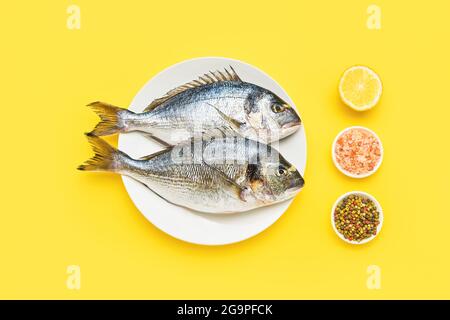 Roher dorado-Fisch auf einem weißen Teller auf gelbem Hintergrund. Mediterranes Meeresfrüchtekonzept. Draufsicht, Platz für Text kopieren Stockfoto