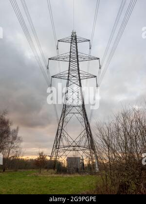 Sonnenuntergang hinter einem Strommast in einer ländlichen Gegend mit einem Mobilfunkmast oben. Stockfoto