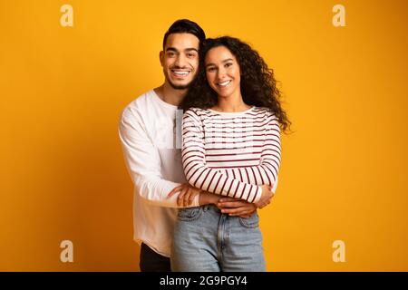 Porträt eines fröhlichen jungen arabischen Paares, das die Kamera umarmt und lächelt Stockfoto