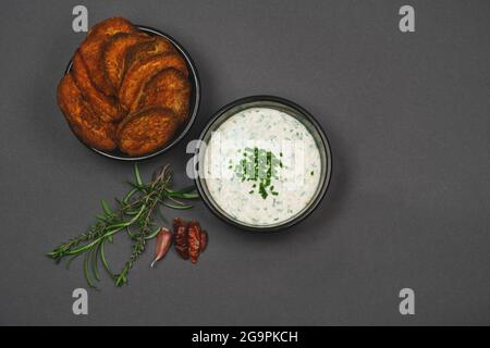 Arial Ansicht von würzigen Süßkartoffeln Snack garniert mit Chili, Rosmarin und Thymian und Joghurt Knoblauch Schnittlauch Dip Sauce in schwarzen Schalen Stockfoto