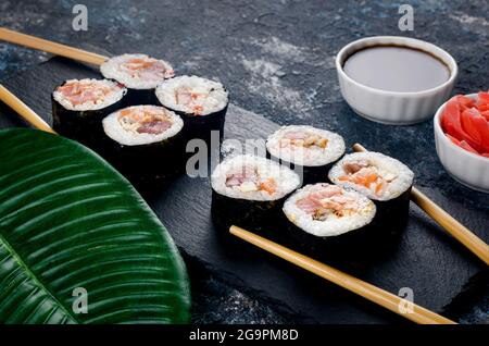 japanisches Sushi-Essen. Maki und Rollen mit Thunfisch in Holzstäbchen auf dunklem Hintergrund. Sushi-Menü. Lieferservice Stockfoto