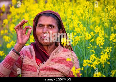 TIKAMGARH, MADHYA PRADESH, INDIEN - 16. JULI 2021: Glückliche alte indische Frau, die im Senffeld steht. Stockfoto