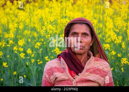 TIKAMGARH, MADHYA PRADESH, INDIEN - 16. JULI 2021: Glückliche alte indische Frau, die im Senffeld steht. Stockfoto