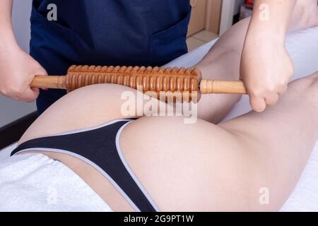 Madero-Therapie Anti-Cellulite-Massage, Lymphdrainage-Massage - die Masseuse massiert den Muskel des hinteren Oberschenkels der Frau mit einem hölzernen m Stockfoto