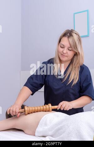 Die hübsche Masseurin massiert den Rücken des Patienten mit einem Holzwalzenmassager. Frau mit Spa-Massage im Schönheitssalon. Stockfoto