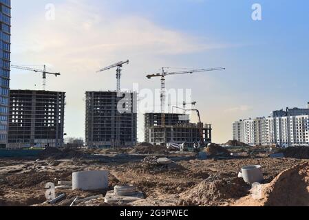 Verlegung von Kanalbrunnen und Rohrleitungen der Heizungsanlage auf der Baustelle. Turmdrehkrane in Aktion. Formarbeiten und Betongießen durch eine сoncrete-Pumpe Stockfoto