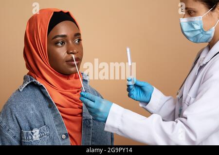 Medizinisches Personal, das einen Tupfer für eine Coronavirus-Probe von einer muslimischen Frau nahm Stockfoto