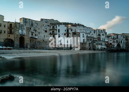 Sonnenaufgang im Hafen von Cefalu, Sizilien, Italien, Altstadt Panoramablick mit bunten Häusern am Wasser, Meer und La Rocca Klippe.attraktiver Sommer Stockfoto