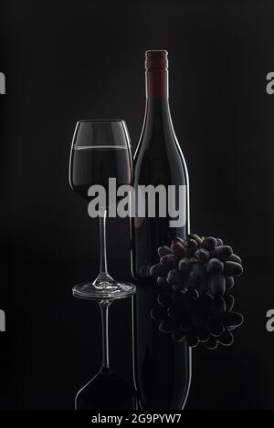 Fotografie von Rotwein in einem Glas auf schwarzem Hintergrund, Flasche, Trauben Stockfoto