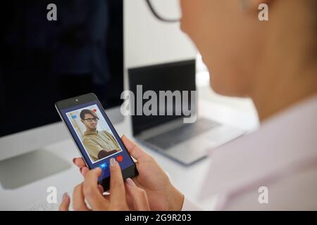 Nahaufnahme einer jungen Frau, die in der Dating-App auf dem Mobiltelefon durch Profile von Männern blättert. Stockfoto