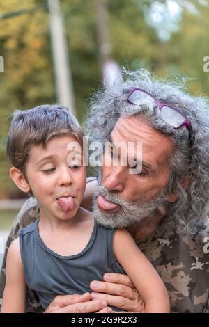 Porträt eines Vaters mit langen grauen Haaren und Sohn zeigen die Zunge im Freien Stockfoto