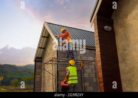 Dachdecker Bauarbeiter installieren neues Dach, Dachdeckwerkzeuge, elektrische Bohrer auf neuen Dächern mit Metallblech verwendet. Stockfoto