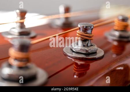 Gitarrenkopf mit Stimmköpfen. Musikinstrumente und Musikkunstkonzept. Selektiver Fokus auf die Stifte mit den Saiten Wind auf. Nahaufnahme. Stockfoto