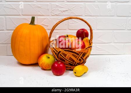 Orangefarbene Kürbisse mit Äpfeln und Birnen in einem Weidenkorb auf weißem Hintergrund. Stillleben im Herbst. Stockfoto