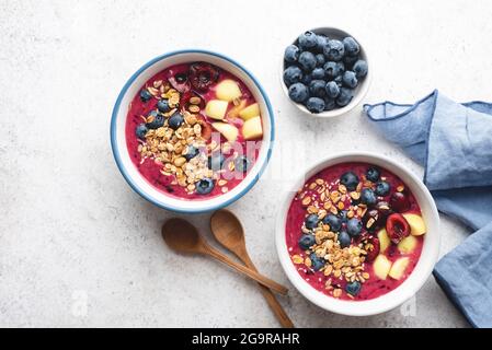 Violette vegane Smoothie-Schale mit Heidelbeeren, Kirschen, Pfirsich und Müsli auf grauem Zementhintergrund, Draufsicht, Kopierraum. Sauberes Esskonzept Stockfoto