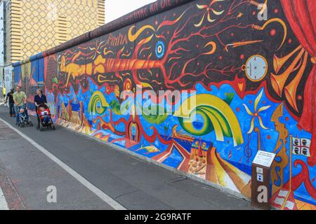 Menschen mit Kinderwagen auf dem Hintergrund von Bildern an der Berliner Mauer. Graffiti in der East Side Gallery. Deutschland, München - 28. April 2011 Stockfoto