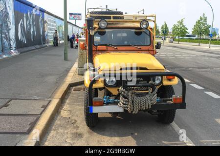 Ein gelber Toyota Land Cruiser steht neben der Berliner Mauer. Graffiti in der East Side Gallery. Deutschland, München - 28. April 2011 Stockfoto