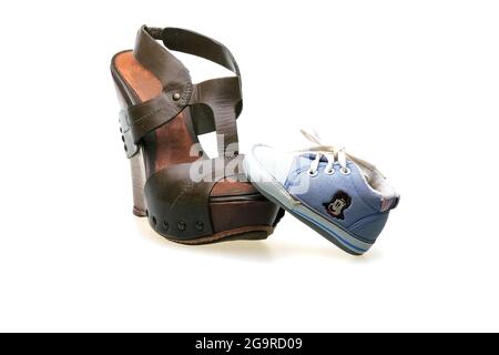 Eine braune Ledersandale für Frauen mit Korksohlen und ein blauer Sneaker für Kinder. Schuhe isoliert auf weißem Hintergrund. Stockfoto