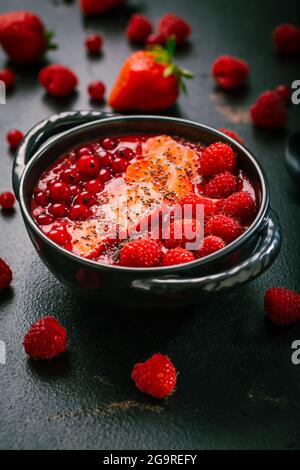 Frühstücksschale mit roten Smoothie-Schalen mit Chiasamen, Erdbeere, Himbeere und roten Johannisbeeren auf schwarzem Hintergrund Stockfoto