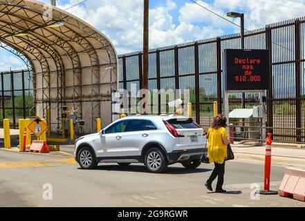 Eine Frau auf dem Fußgängerüberweg an der US-mexikanischen Grenze mit einem digitalen Schild auf Spanisch, das die Notwendigkeit ankündigt, bei der Einreise an der Grenze mehr als 10.000 Personen zu melden Stockfoto