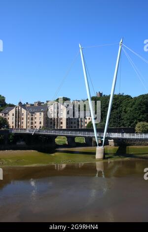 Millennium Bridge über den Fluss Lune in Lancaster, Lancashire, England mit neuen Apartmentgebäuden an der Damside Street und der Priory Church an der Skyline. Stockfoto