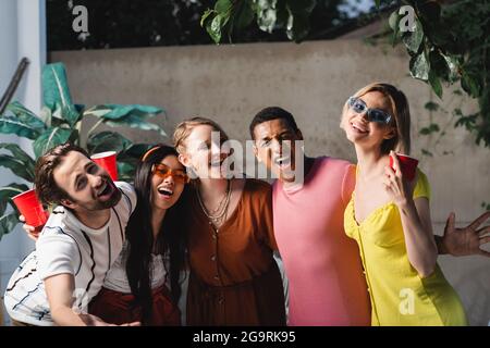 Fröhliche multiethnische Freunde mit Plastikbechern, die Spaß im Freien haben Stockfoto