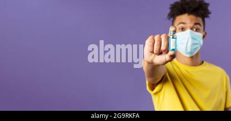 Medizin, Coronavirus und Menschen Konzept. Nahaufnahme des jungen Mannes in der Gesichtsmaske, die Ampulle mit dem Medikament hält, schließlich Impfstoff aus Kovid19 gefunden Stockfoto