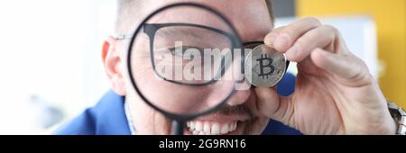 Der Mensch schaut durch die Lupe und hält Bitcoin in seinem Hand Stockfoto