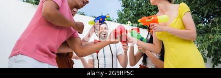 Aufgeregt multikulturelle Freunde mit Wasserpistolen Toasten mit Plastikbechern während der Party, Banner Stockfoto