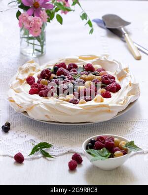 Pavlova-Kuchen mit Creme und Beeren und einem Blumenstrauß auf hellem Hintergrund. Stockfoto