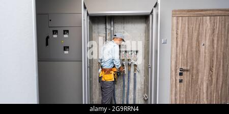 Männlicher Klempner prüft Rohre für zentrale heiß- und Kaltwasserversorgung der Wohnung Stockfoto