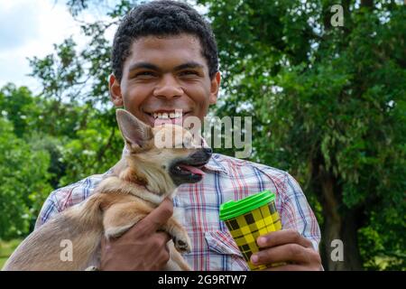 Afroamerikanischer Mann hält einen chihuahua Hund und trinkt Kaffee aus einer Einweg-Tasse Stockfoto