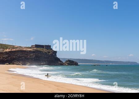 Nazare, Portugal - 29. Juni 2021: Ein Surfer am North Beach spaziert unterhalb der Festung Nazare ins Meer Stockfoto