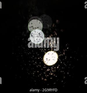 Lichter und Bokeh durch das Autofenster mit Regentropfen. Stockfoto