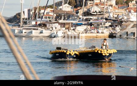 Tribunj, Kroatien - 1. Juli 2021: Mann steuert ein Fischerboot mit gelben Kotflügelbojen am Sommertag am Hafen Stockfoto