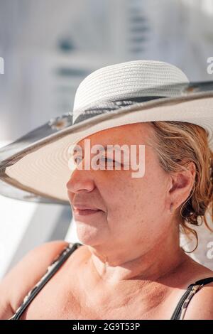 Eine Frau in einem Strohhut. Profilporträt einer charmanten Frau in einem weißen Strohhut, die sich am Strand am Meer im Schatten entspannt Stockfoto