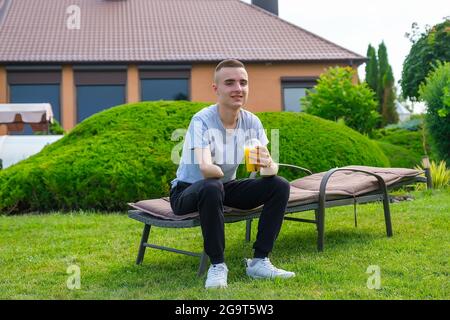 Ein Mann mit einem amputierten Arm sitzt auf einer Sonnenliege und trinkt einen Cocktail im Garten Stockfoto