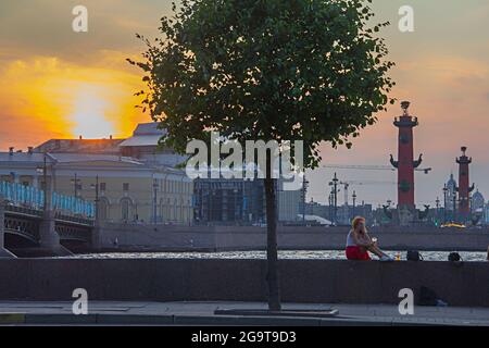 Sankt-Petersburg, Russland - am 7. Juli 2021 sitzt ein nettes Mädchen spät in der weißen Nacht auf der Brüstung bei Sonnenuntergang in der Nähe des Flusses Neva Stockfoto