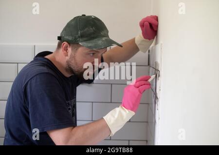 Arbeiter trägt graue Fugen auf weißen Fliesen mit Gummikelle auf. Stockfoto